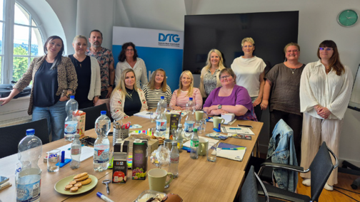 Gruppenfoto stehend hinter einem großen Tagungs-Tisch