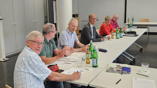 Personen sitzen an einem U-förmigen Tisch