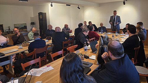 Tische in U-Form mit Zuhörern, in der Mitte der Redner Kai Rosenberger