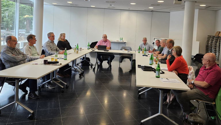 Mehrere Personen sitzen an einem U-förmigen Tisch