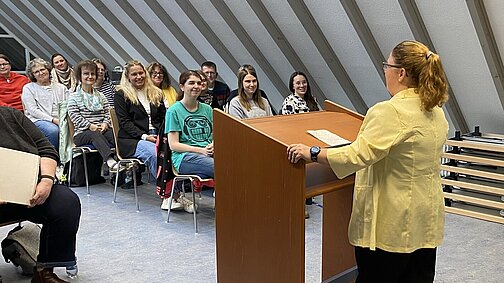 Blick in den Saal mit Teilnehmerinnen und Teilnehmern und Rednerin am Rednerpult von hinten